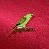 An enamel Swift Parrot pin affixed to red fabric.