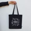 A hand holding a black tote bag featuring white illustrations from the Aussie Bird Count website.