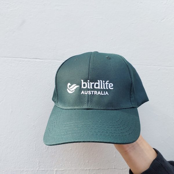 A bottle green coloured cap featuring a white embroidered BirdLife Australia logo, photographed in front of a neutral background.
