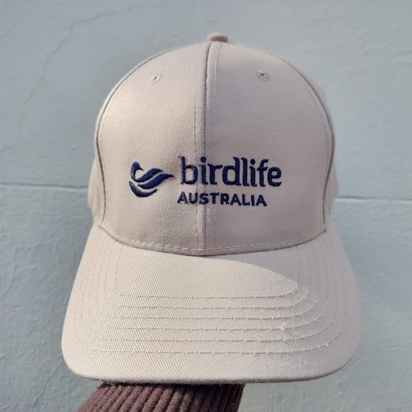 A stone coloured cap featuring a navy embroidered BirdLife Australia logo, photographed in front of a neutral background.